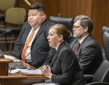 Katrina Gulstad sits at the testifiers' table and speaks to someone out of view. Jim Hegman and Representative Xiong sit next to her.